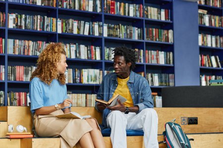 Téléchargez les photos : Portrait de deux collégiens bavardant dans un cadre de bibliothèque dynamique avec ton bleu, espace de copie - en image libre de droit