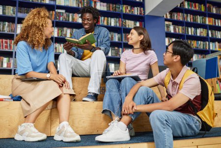 Téléchargez les photos : Plan complet d'étudiants multiethniques étudiant ensemble dans la bibliothèque avec des couleurs bleues vibrantes - en image libre de droit