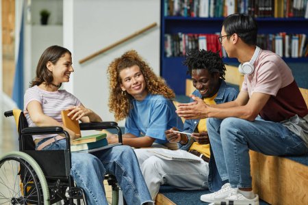 Foto de Diverso grupo de jóvenes charlando en la biblioteca de la universidad, incluyendo una estudiante con discapacidad - Imagen libre de derechos