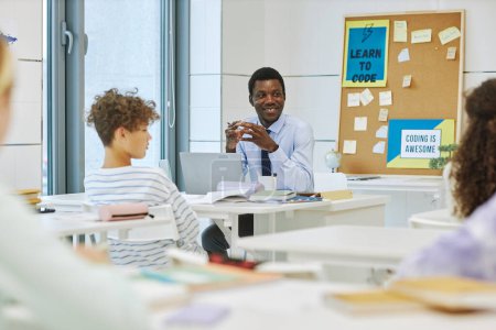 Téléchargez les photos : Portrait d'homme noir souriant comme professeur avec des enfants dans la salle de classe, espace de copie - en image libre de droit