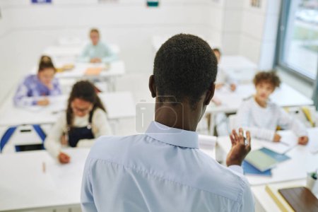 Téléchargez les photos : Vue arrière minimale de l'enseignant masculin amenant à divers groupes d'enfants en classe - en image libre de droit