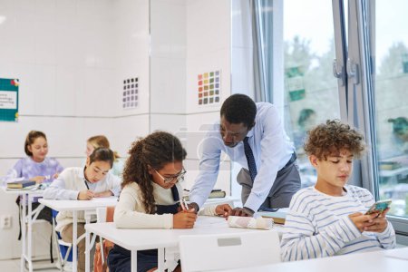 Photo for Portrait of black male teacher working with children taking test in school classroom - Royalty Free Image