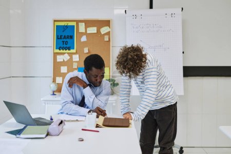 Photo for Portrait of young black teacher helping boy with task or grading homework in school classroom - Royalty Free Image