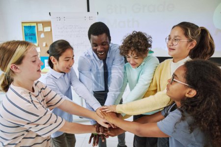 Photo for High angle portrait of diverse schoolchildren huddling in team exercise in classroom and stacking hands - Royalty Free Image
