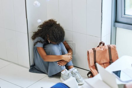 Téléchargez les photos : Vue grand angle de jeune fille noire harcelée à l'école et assise sur le sol avec écouteurs - en image libre de droit