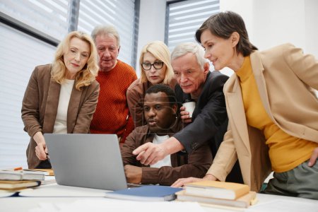 Foto de Grupo de personas mayores que aprenden un nuevo programa de computadora portátil junto con el profesor en el escritorio en el aula - Imagen libre de derechos
