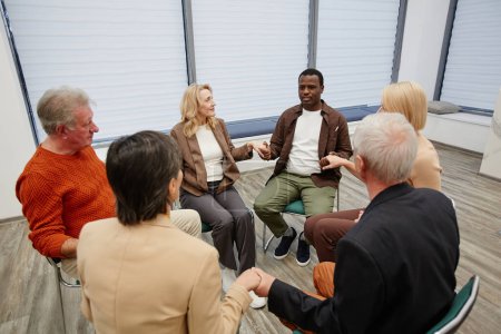Téléchargez les photos : Groupe de personnes âgées assises sur des chaises en cercle et tenant la main avec psychologue pendant la psychothérapie - en image libre de droit