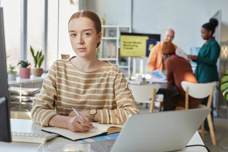 Foto de Retrato de una joven experta mirando la cámara mientras está sentada en el escritorio en la oficina de la compañía, espacio para copiar - Imagen libre de derechos