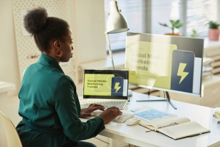 Téléchargez les photos : Portrait latéral de jeune femme d'affaires noire utilisant un ordinateur tout en travaillant avec des données marketing dans le bureau, espace de copie - en image libre de droit
