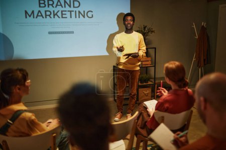 Photo for Portrait of young black man giving presentation on brand marketing to team while standing by projector screen and addressing audience in business training - Royalty Free Image