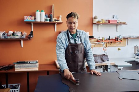 Foto de Retrato de cintura hacia arriba del joven artesano que trabaja con cuero en el estudio y crea piezas hechas a mano, espacio para copiar - Imagen libre de derechos