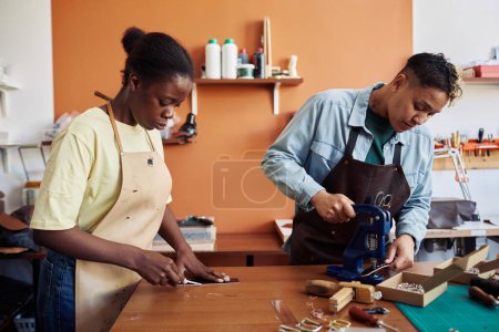 Photo for Side view portrait of two multiethnic young women working with leather in workshop and creating handmade pieces - Royalty Free Image