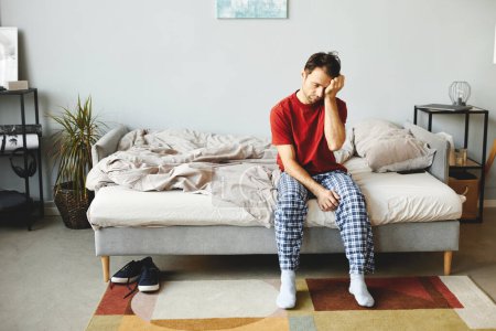 Téléchargez les photos : Jeune homme assis sur son lit se réveillant le matin à la maison - en image libre de droit