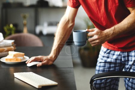 Foto de Primer plano del joven bebiendo café por la mañana y usando la computadora en la mesa - Imagen libre de derechos