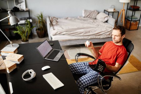 Téléchargez les photos : Jeune homme assis sur une chaise avec gant de baseball et balle et regarder le jeu de sport sur ordinateur pendant les loisirs à la maison - en image libre de droit