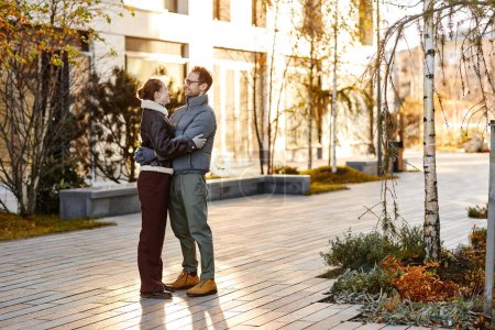 Téléchargez les photos : Jeune couple s'embrassant debout dans la rue et profitant de leur promenade le jour d'automne - en image libre de droit