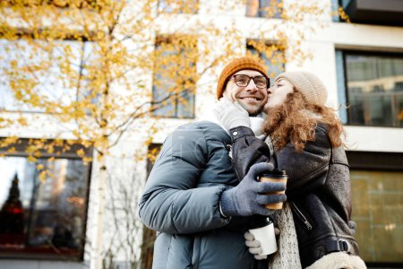 Photo for Young woman kissing her boyfriend during their walk in the city in autumn day - Royalty Free Image