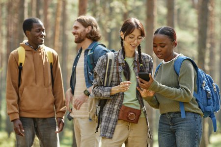 Foto de Chicas jóvenes utilizando el navegador en el teléfono móvil, mientras que de pie en el bosque durante su viaje - Imagen libre de derechos