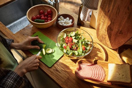 Photo for Close-up of girl cutting fresh vegetables on cutting board for salad at wooden table in the van - Royalty Free Image