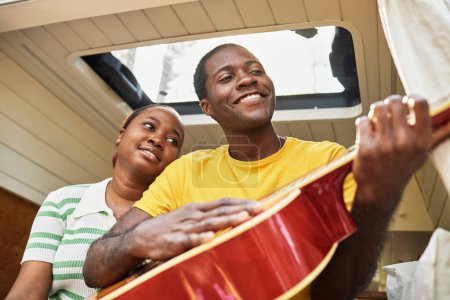 Téléchargez les photos : Jeune couple africain jouant de la guitare assis dans la maison des roues - en image libre de droit
