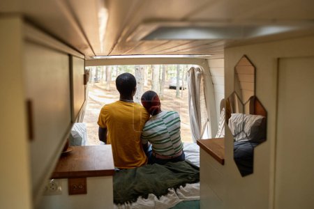 Foto de Vista trasera de la joven pareja africana disfrutando de la naturaleza juntos mientras están sentados en la cama y abrazándose en la autocaravana - Imagen libre de derechos