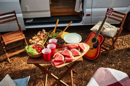 Téléchargez les photos : Vue en angle élevé de la table avec fruits et salade sur pique-nique dans la nature pendant le camping dans la forêt - en image libre de droit