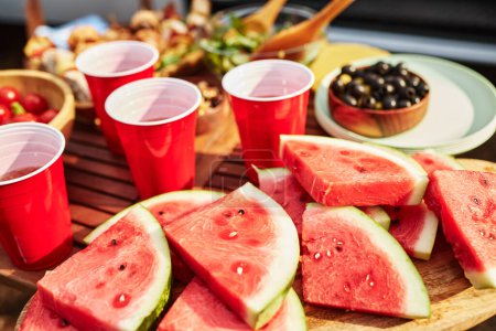 Photo for Close-up of sweet watermelon with drinks on table preparing for picnic outdoors - Royalty Free Image