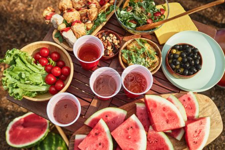 Téléchargez les photos : Vue en angle élevé de la table en bois avec salade, fruits et boissons pour pique-nique en plein air - en image libre de droit
