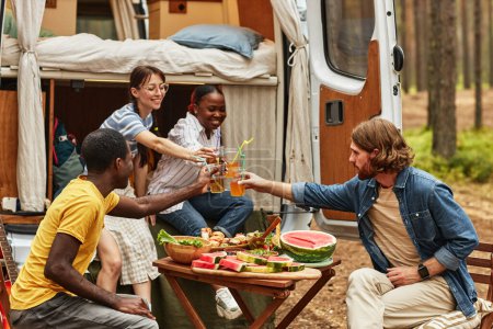 Photo for Group of young friends toasting for their rest with drinks while sitting on picnic outdoors during camping with motorhome - Royalty Free Image