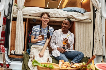 Téléchargez les photos : Portrait de deux jeunes filles buvant des cocktails et souriant à la caméra alors qu'elles étaient assises en camping-car pendant le camping - en image libre de droit