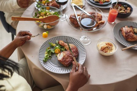 Téléchargez les photos : Vue ci-dessus de la famille africaine manger du poulet rôti avec salade de légumes à table pendant le dîner de vacances - en image libre de droit