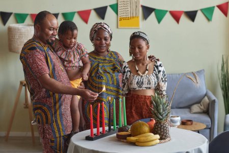 Téléchargez les photos : Famille africaine de quatre bougies allumées ensemble pour célébrer les vacances de Kwanzaa ensemble à la maison - en image libre de droit