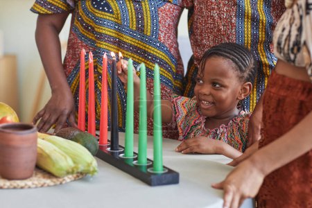 Afrikanisches kleines Kind brennt Kerzen für Kwanzaa Feiertag, um mit ihrer Familie zu feiern