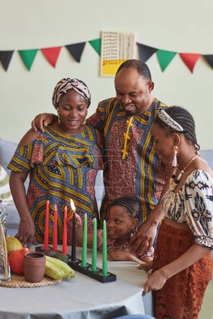 Afrikanische vierköpfige Familie umarmt und lächelt, während kleines Mädchen Kerzen für den Kwanzaa-Urlaub anzündet