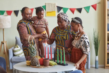 Familia africana de cuatro celebrando Kwanzaa en casa, encendieron siete velas juntas en la mesa