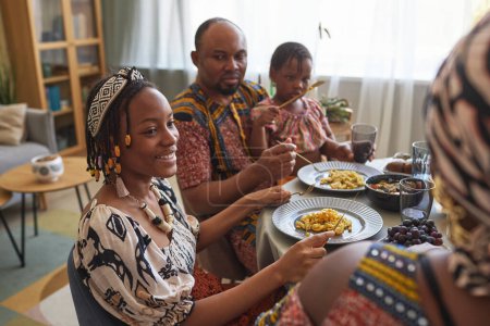 Téléchargez les photos : Africaine heureuse fille parler à sa famille pendant le dîner de vacances à la table à la maison - en image libre de droit