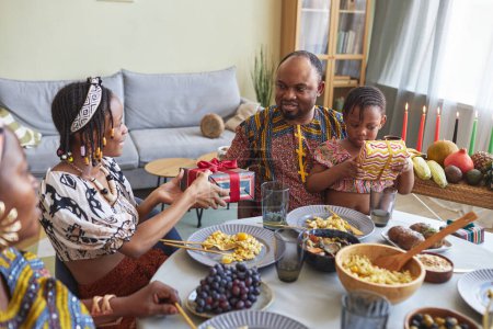 Foto de Familia africana dando regalos el uno al otro durante la cena de vacaciones en la mesa en casa, que celebran Kwanzaa - Imagen libre de derechos