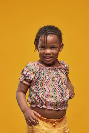 Foto de Retrato de niña africana sonriendo a la cámara de pie sobre fondo amarillo - Imagen libre de derechos