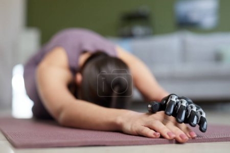 Téléchargez les photos : Gros plan de la jeune femme avec prothèse bras faisant des exercices d'étirement sur tapis d'exercice à la maison - en image libre de droit