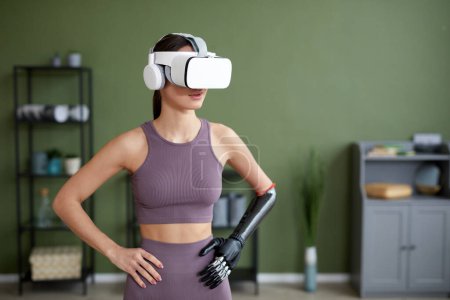 Photo for Young woman with prosthetic arm doing exercises in VR glasses in the room - Royalty Free Image