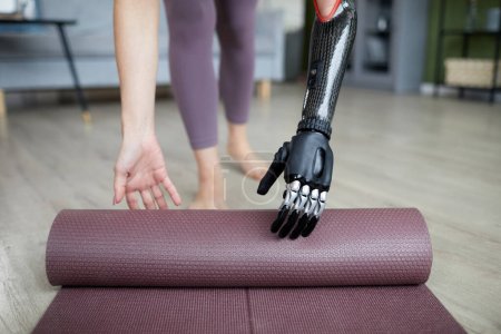 Téléchargez les photos : Gros plan de la jeune femme avec un bras prothétique en utilisant un tapis d'exercice dans son entraînement à la maison - en image libre de droit