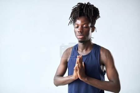 Foto de Retrato de un joven africano meditando con los ojos cerrados de pie sobre un fondo azul - Imagen libre de derechos