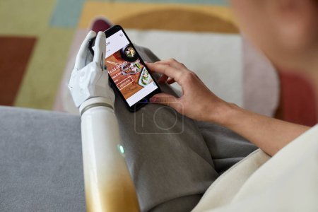 Téléchargez les photos : Gros plan de la jeune femme avec un bras prothétique en utilisant son smartphone pour commander de la nourriture en ligne - en image libre de droit