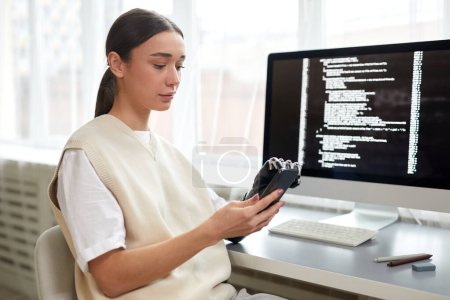 Photo for Young woman with disability using her smartphone at work while sitting at table with computer - Royalty Free Image