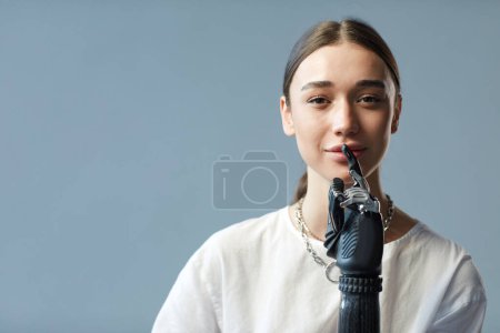 Foto de Retrato de mujer joven con discapacidad que tiene el brazo protésico mirando a la cámara contra el fondo azul - Imagen libre de derechos