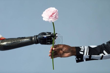 Téléchargez les photos : Gros plan de l'homme africain donnant des fleurs à une femme avec un bras prothétique isolé sur fond bleu - en image libre de droit