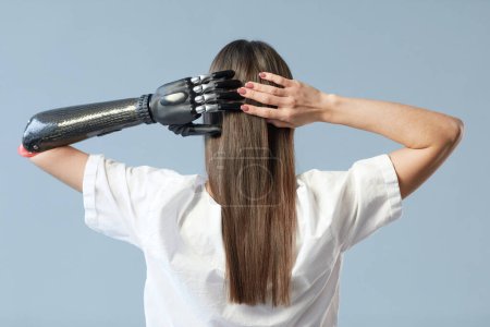 Téléchargez les photos : Vue arrière de la jeune fille avec un bras prothétique et les cheveux longs debout sur fond bleu - en image libre de droit