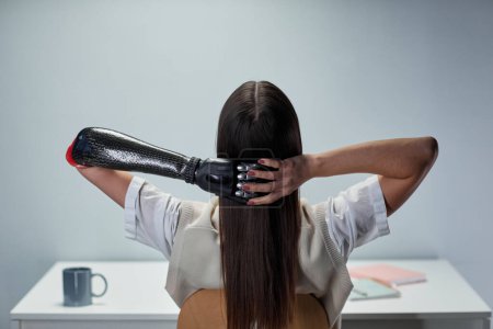 Téléchargez les photos : Vue arrière de la fille avec un bras prothétique reposant à la table après le travail - en image libre de droit