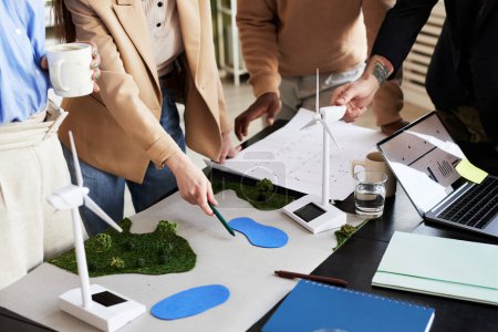 Foto de Primer plano del grupo de arquitectos desarrollando un nuevo proyecto medioambiental con molinos de viento a la mesa - Imagen libre de derechos