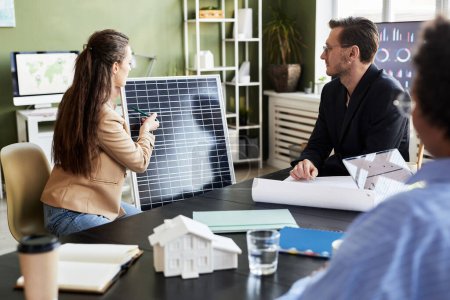 Foto de Joven empresaria presentando nuevo panel solar a sus colegas en la mesa en la reunión, discuten la energía alternativa en equipo - Imagen libre de derechos